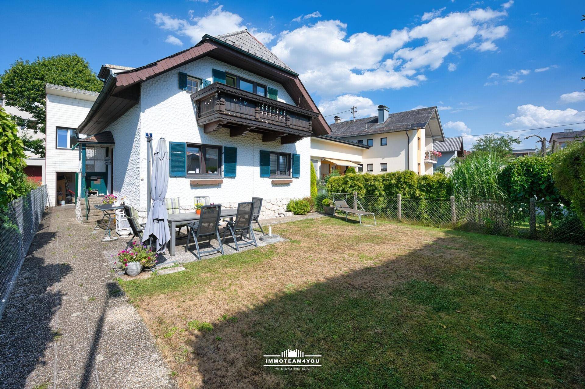 Seitlicher Blick auf den Garten mit Terrasse und Rasenfläche, umgeben von einem Zaun.