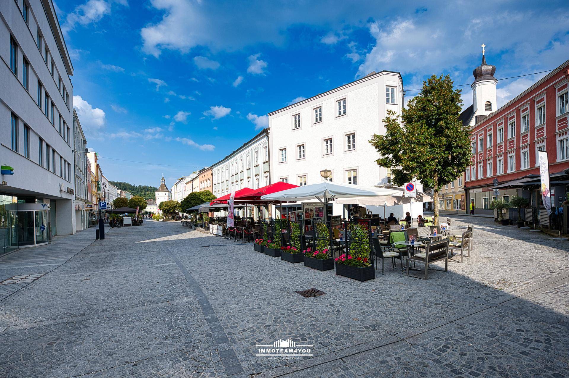 Belebtes Stadtzentrum mit Kopfsteinpflaster, Straßencafés und historischen Gebäuden unter blauem Himmel.