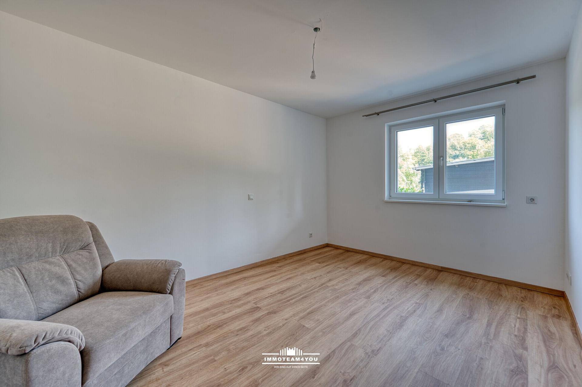 Leeres Schlafzimmer mit Laminatboden und einem Fenster, das viel Tageslicht hereinlässt.