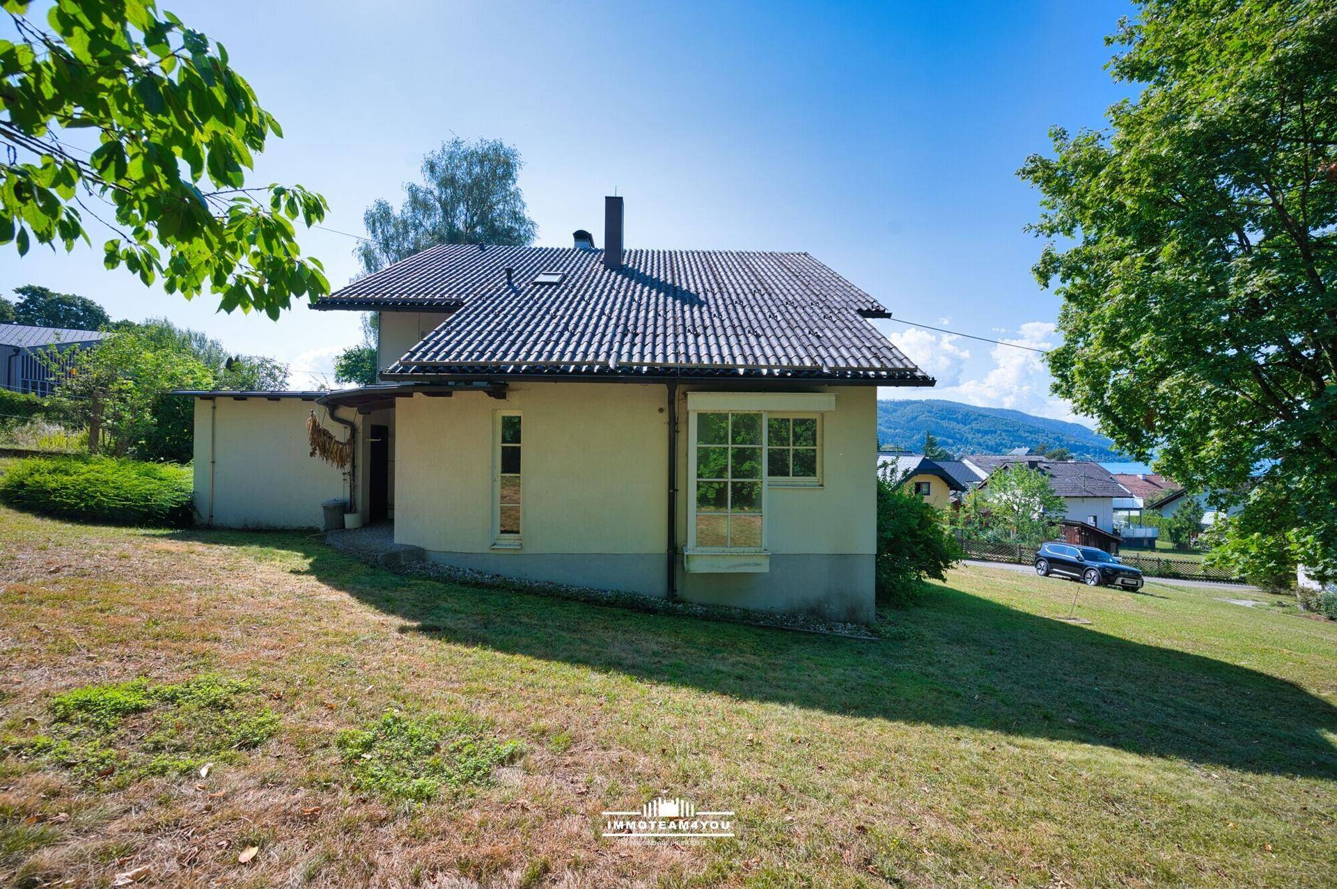 Seitenansicht des Hauses mit weitläufigem Rasenbereich und Blick auf den fernen See.