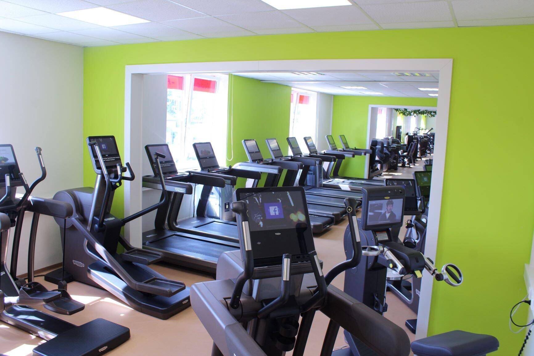 Fitnessraum mit modernen Cardiogeräten und einem großen Spiegel an der Wand für Trainingskontrolle.