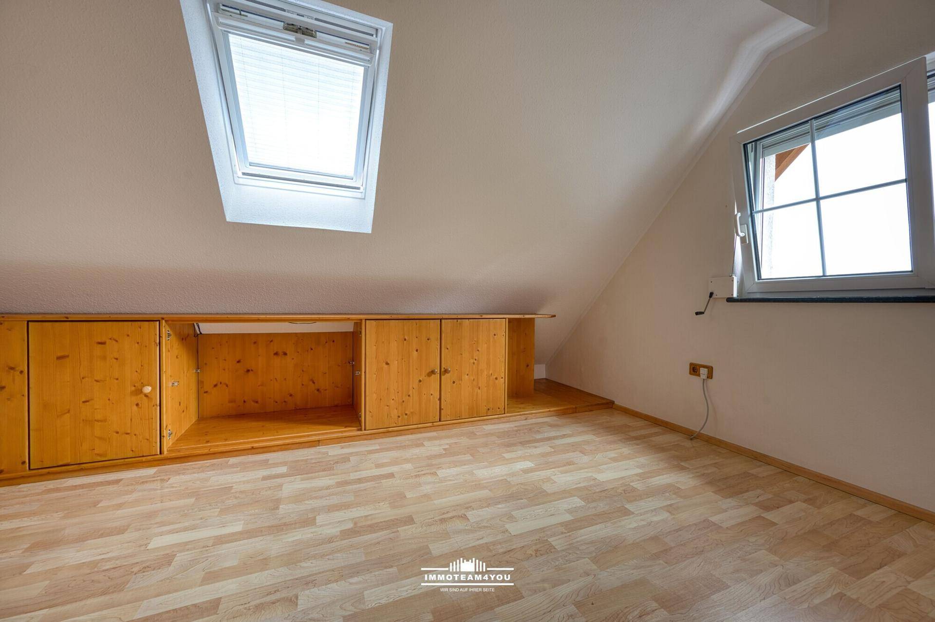 Heller Dachbodenraum mit Holzboden, Dachfenstern und integrierten Holzschränken.