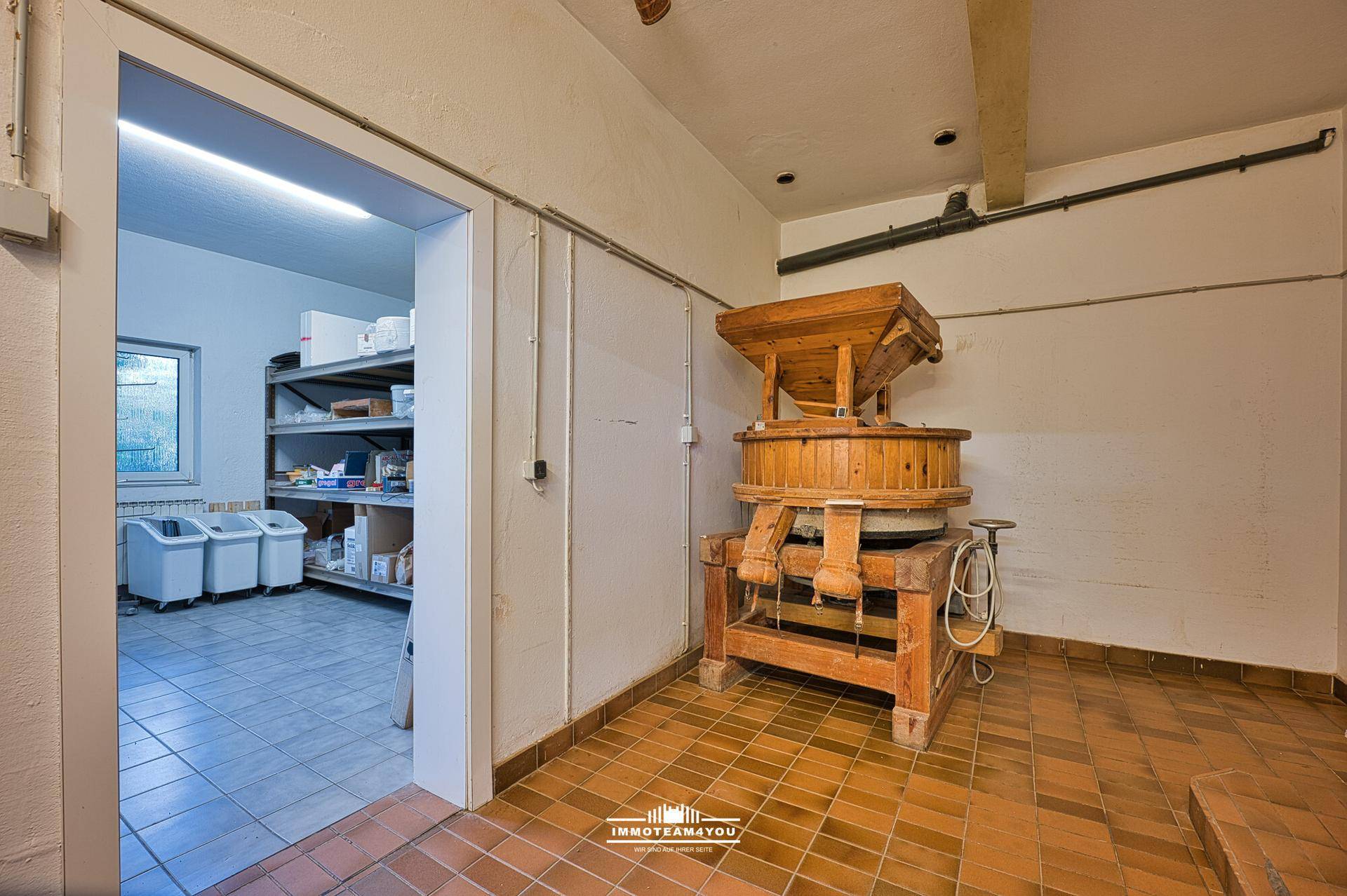Lagerraum mit traditioneller Holzmühle und Regalen für Vorräte, gefliestem Boden.