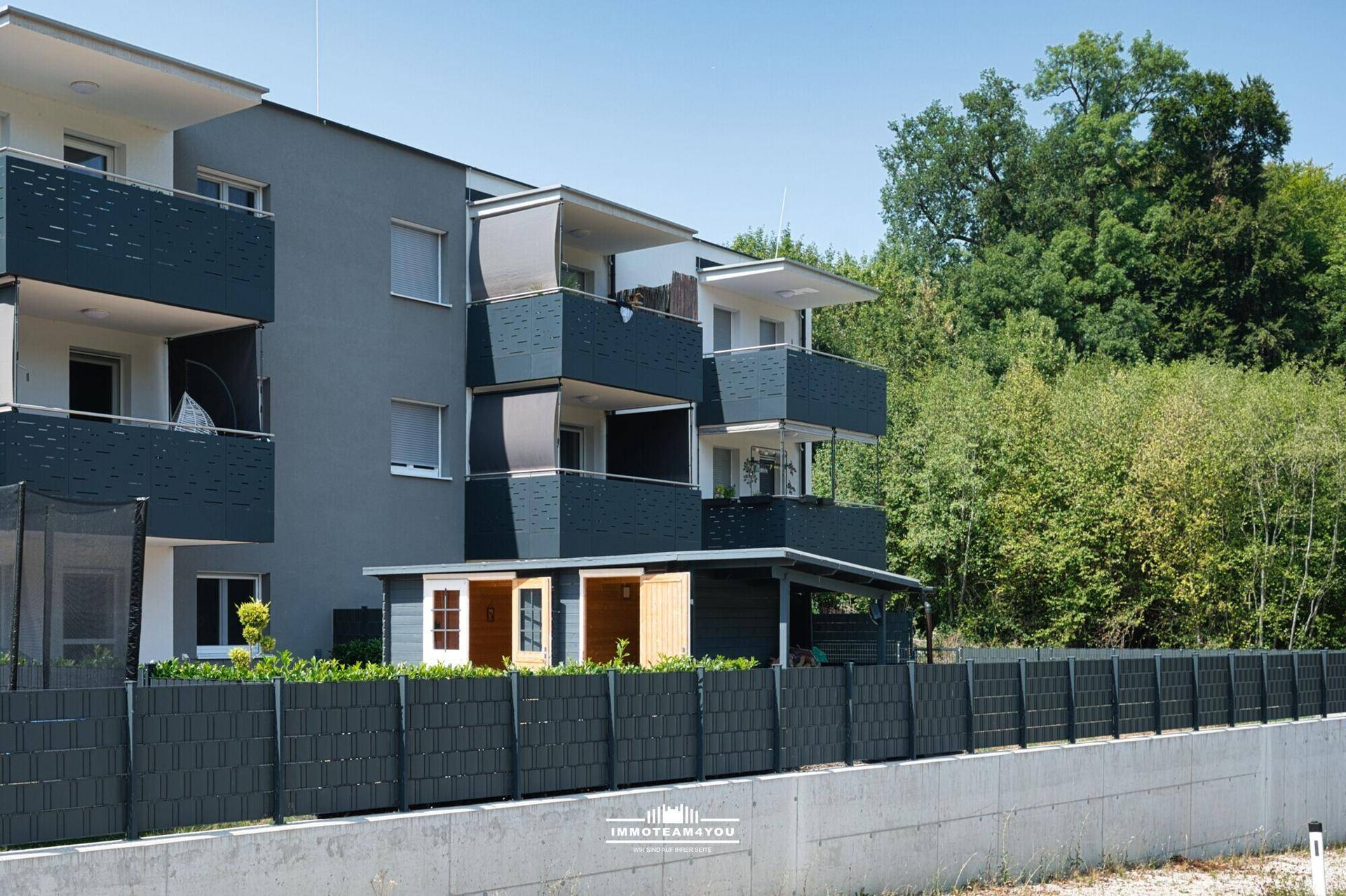 Moderne Wohnhausfassade mit mehreren Balkonen und umgebender grüner Landschaft.