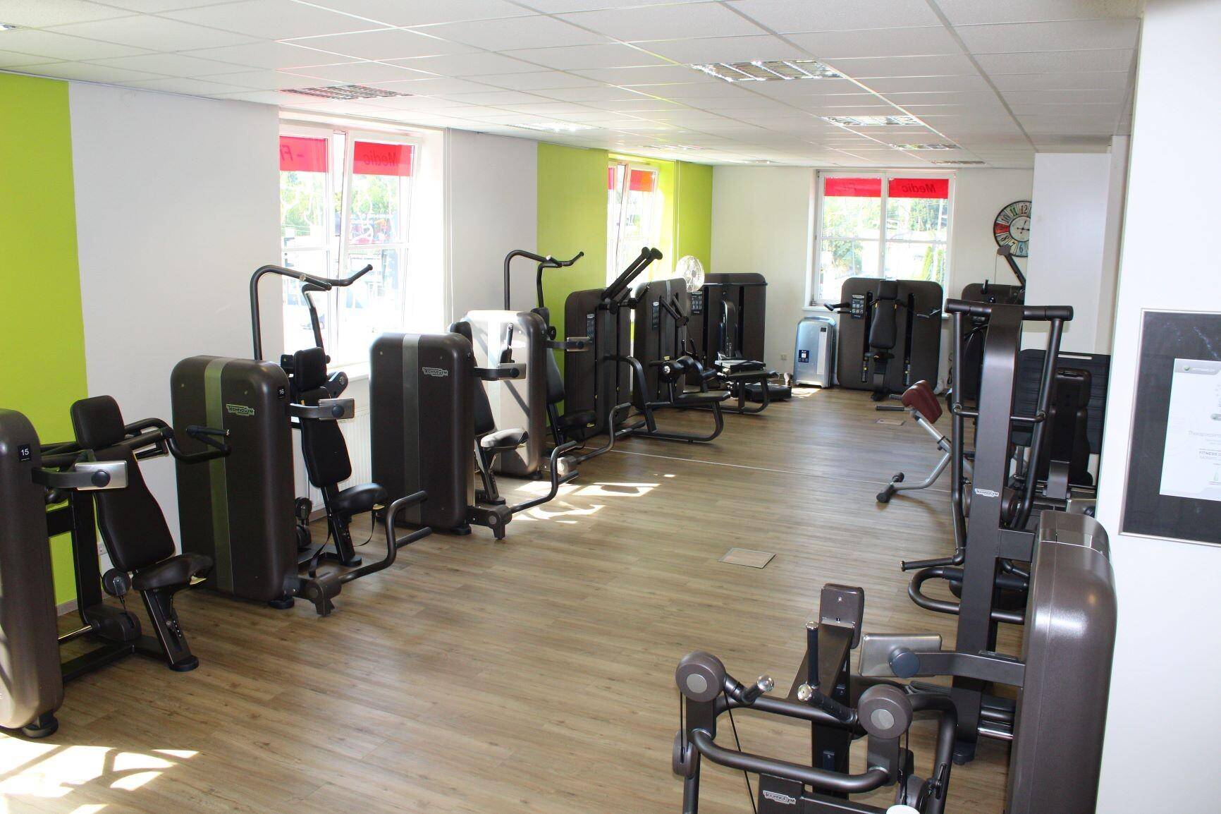 Fitnessraum mit verschiedenen Krafttrainingsgeräten und großen Fenstern für natürliches Licht.
