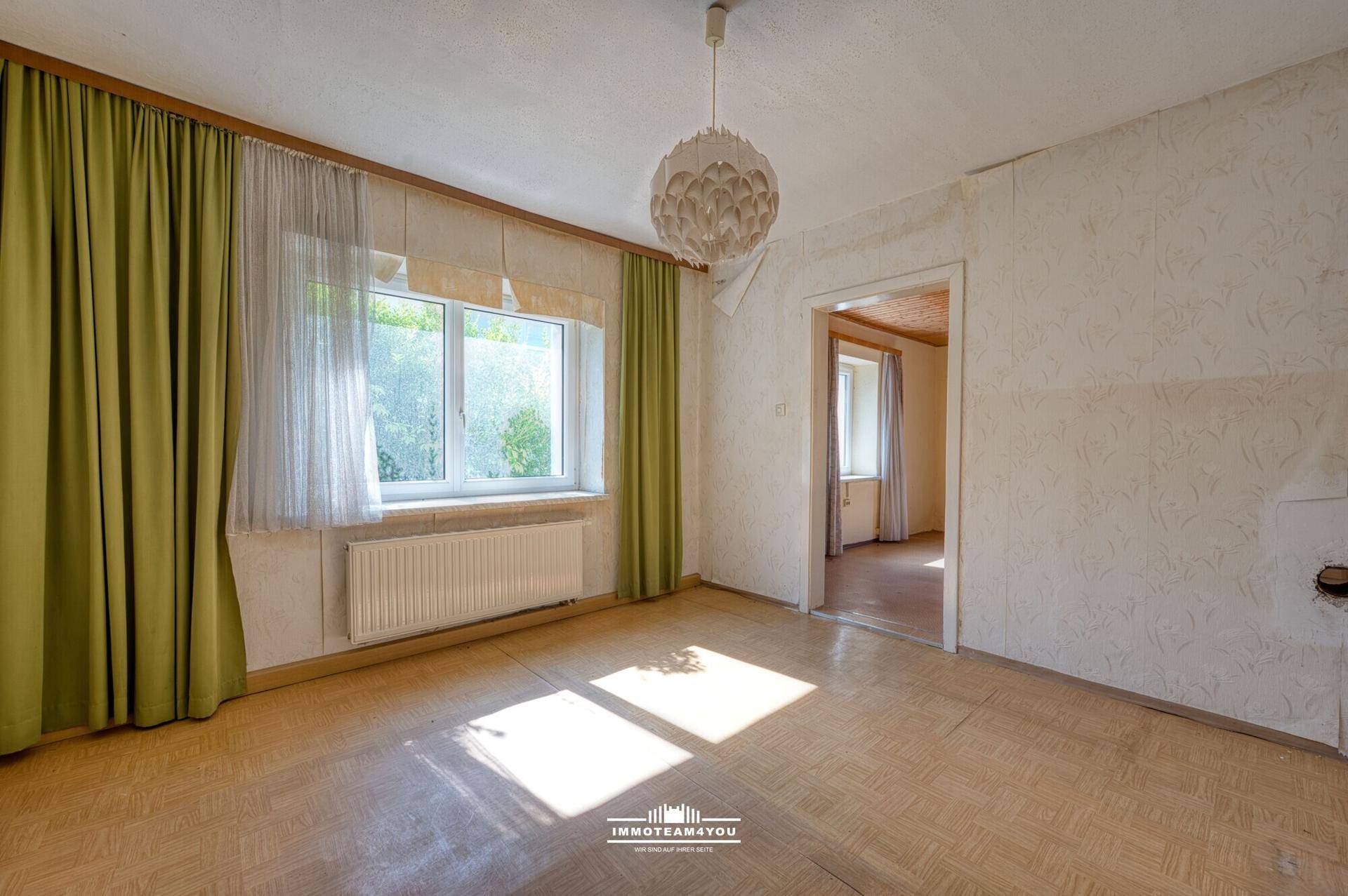Heller Raum mit Fenster, älterem Bodenbelag und Tapetenresten, benötigt Renovierung.