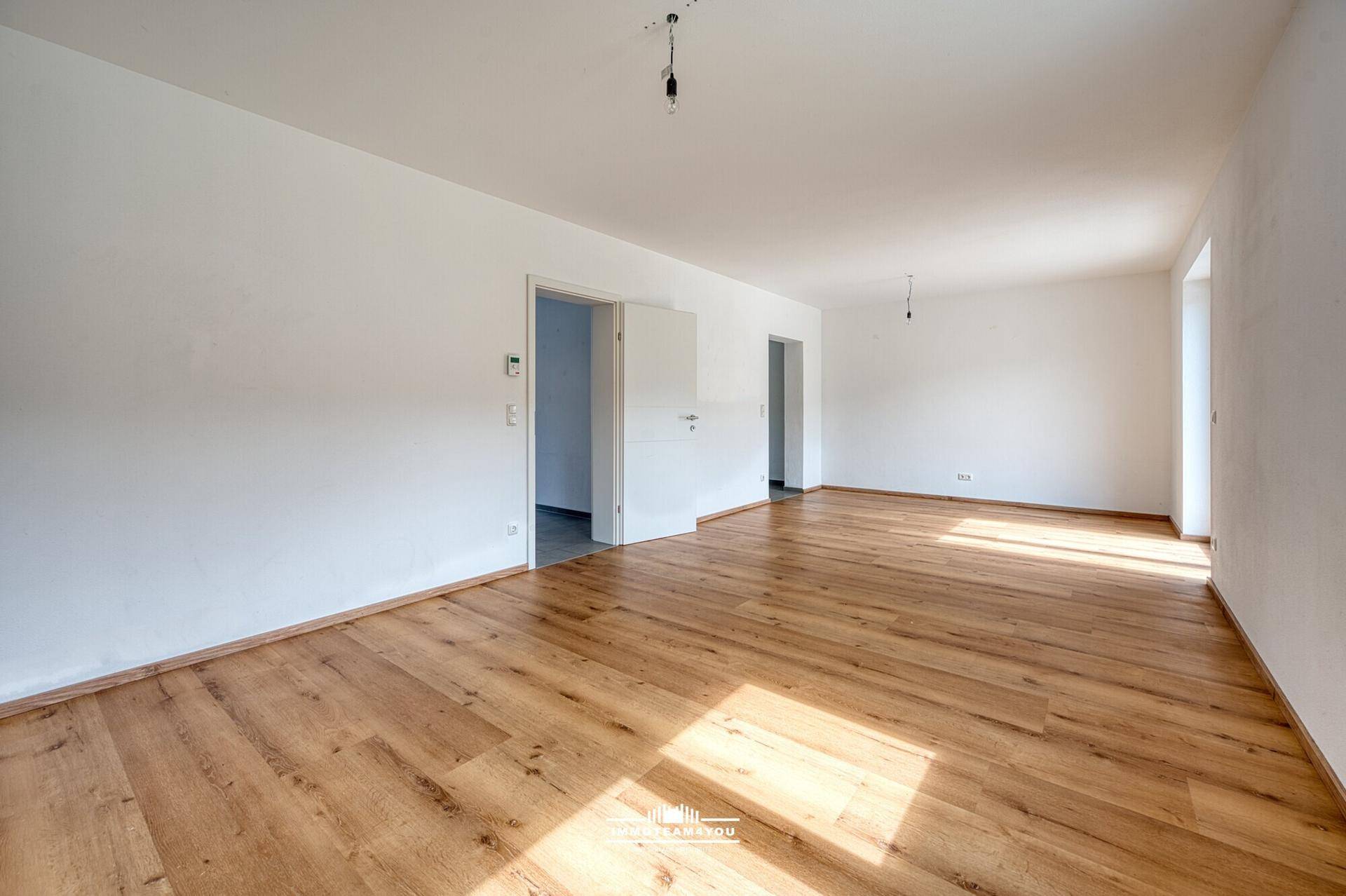 Leeres, lichtdurchflutetes Wohnzimmer mit hellem Holzboden und weißen Wänden, bereit zum Einzug.