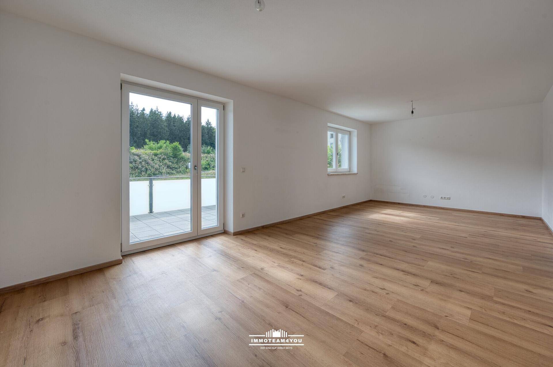 Heller, leerer Raum mit Holzboden und großer Glastür, die auf eine Terrasse führt.