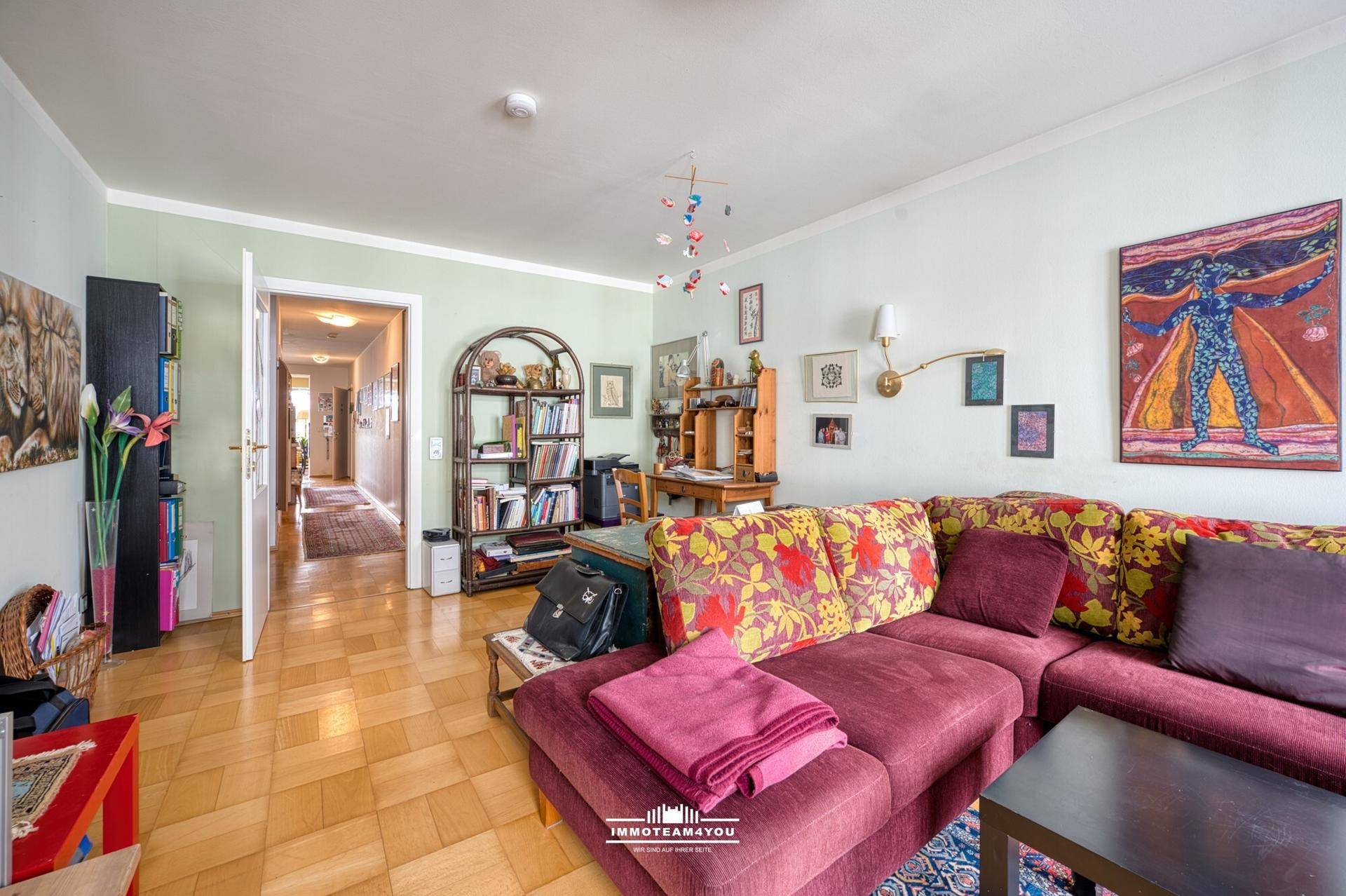 Geräumiges Wohnzimmer mit farbenfrohem Sofa, Bücherregalen und einem Durchgang zum Flur.
