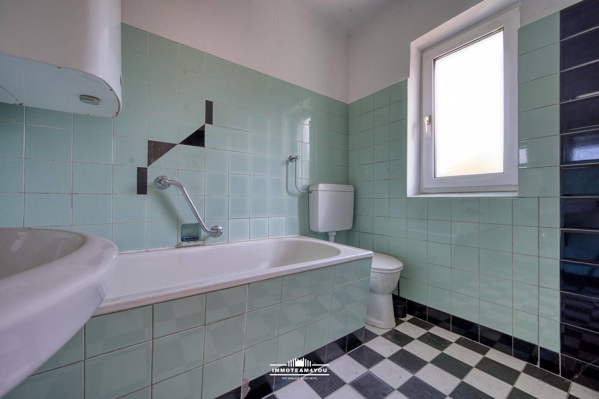 Badezimmer mit Badewanne, WC und mintgrünen Fliesen im Stil der 80er Jahre.