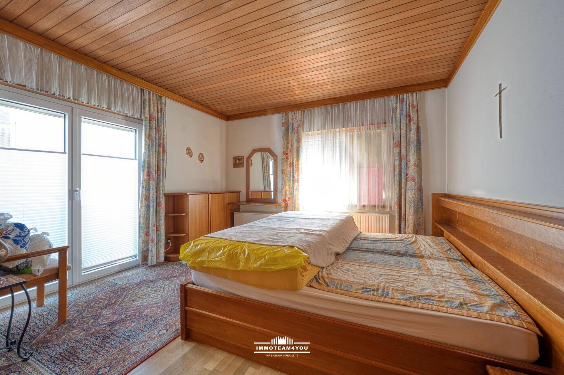 Schlafzimmer mit Doppelbett, Holzdecke und Zugang zu einem Balkon oder großer Fensterfront.