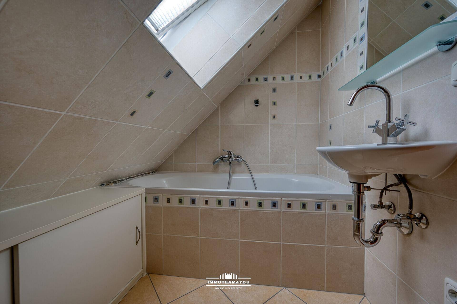 Badezimmer im Dachgeschoss mit Badewanne, Fliesen und Dachfenster.