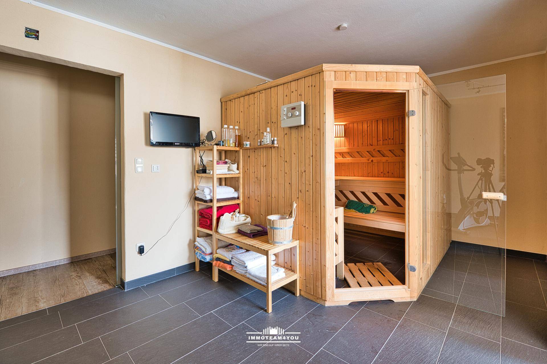 Wellnessbereich mit Holzsauna, Fliesenboden und Ablagemöglichkeiten.