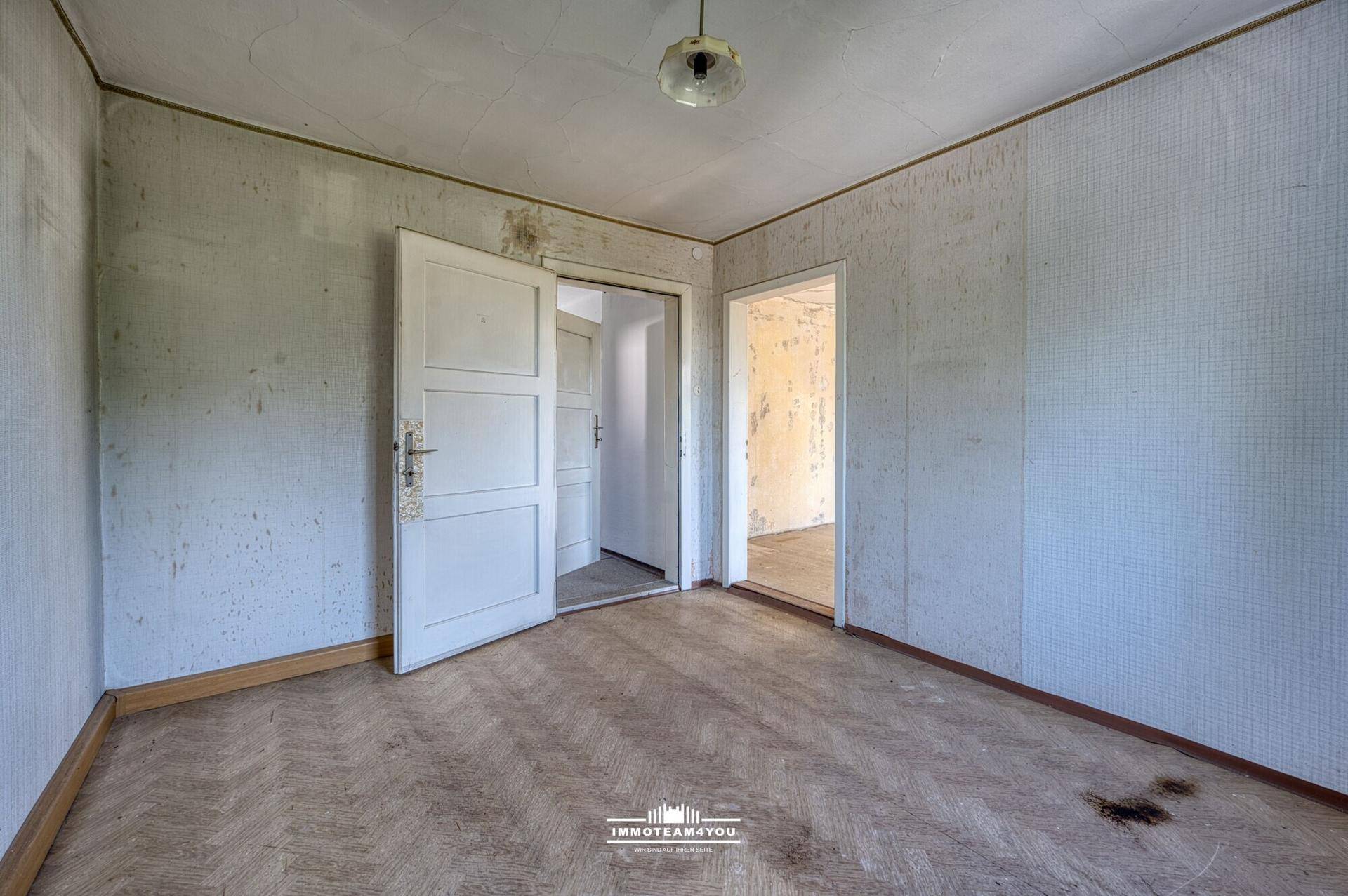 Raum mit Fischgrätparkett und abgenutzten Wänden, ideal für eine Modernisierung.