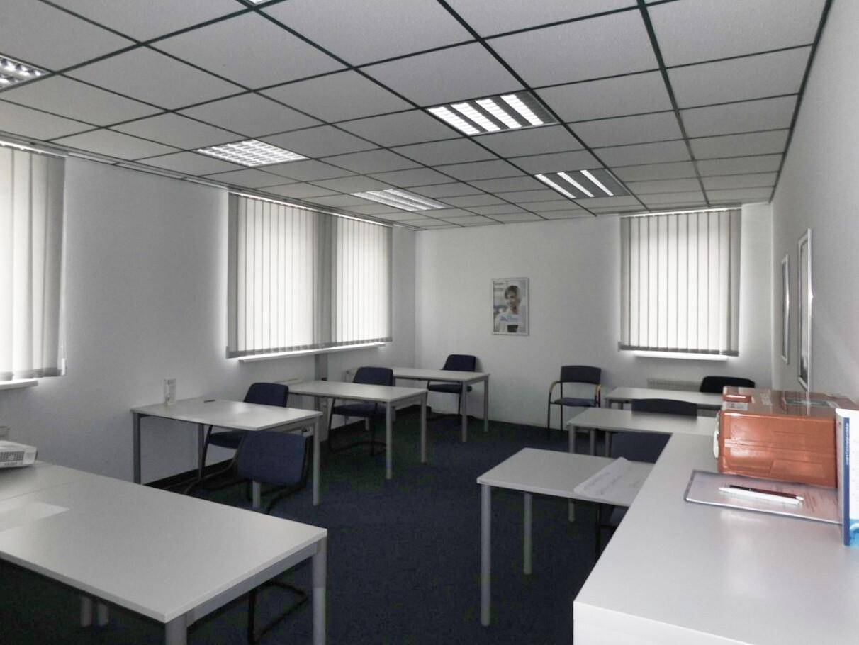Geräumiger Schulungsraum mit mehreren Tischen und Stühlen, ideal für Kurse oder Workshops.
