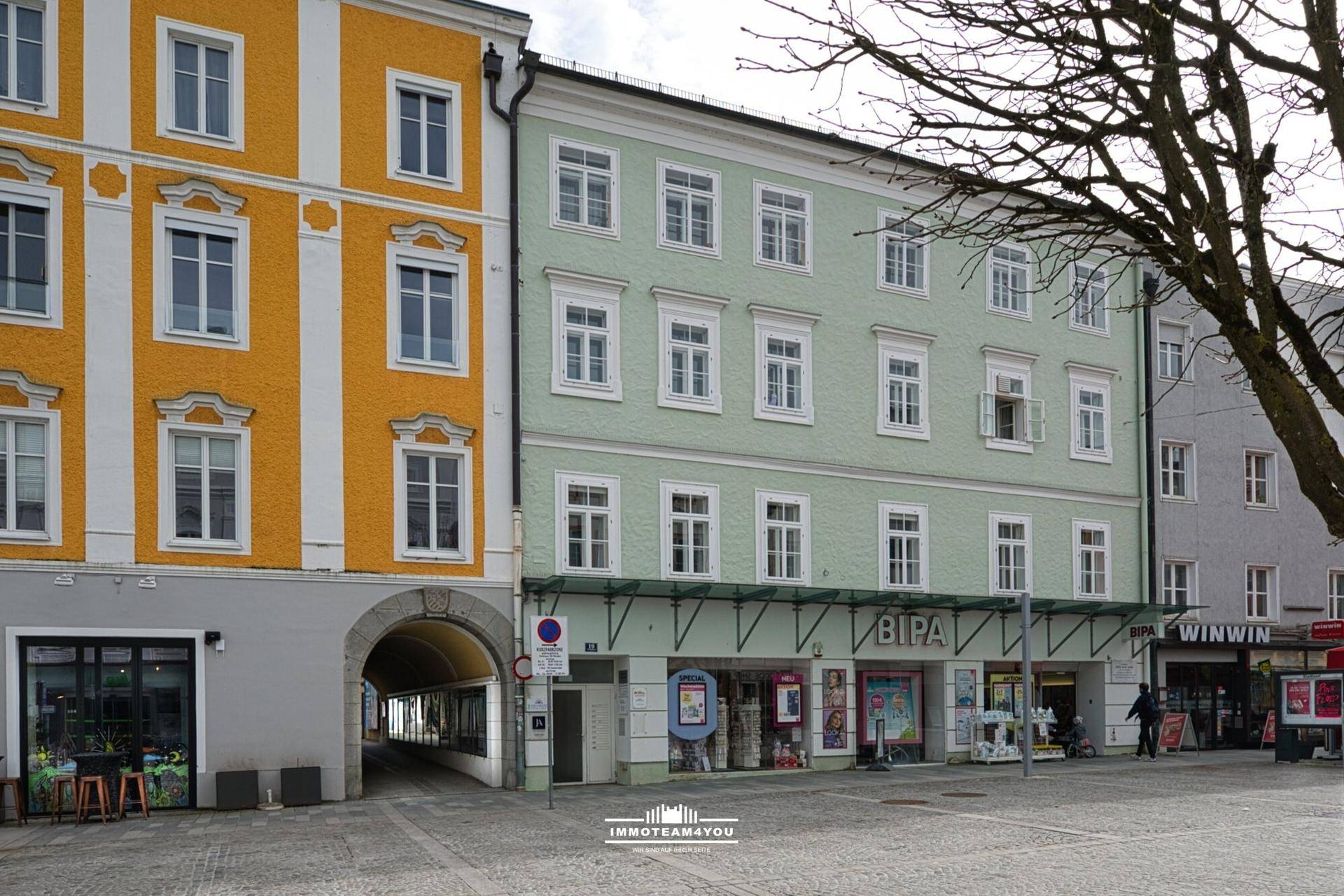 Ansicht eines historischen Gebäudes mit hellgrüner Fassade und einem Durchgang zu einem Innenhof.