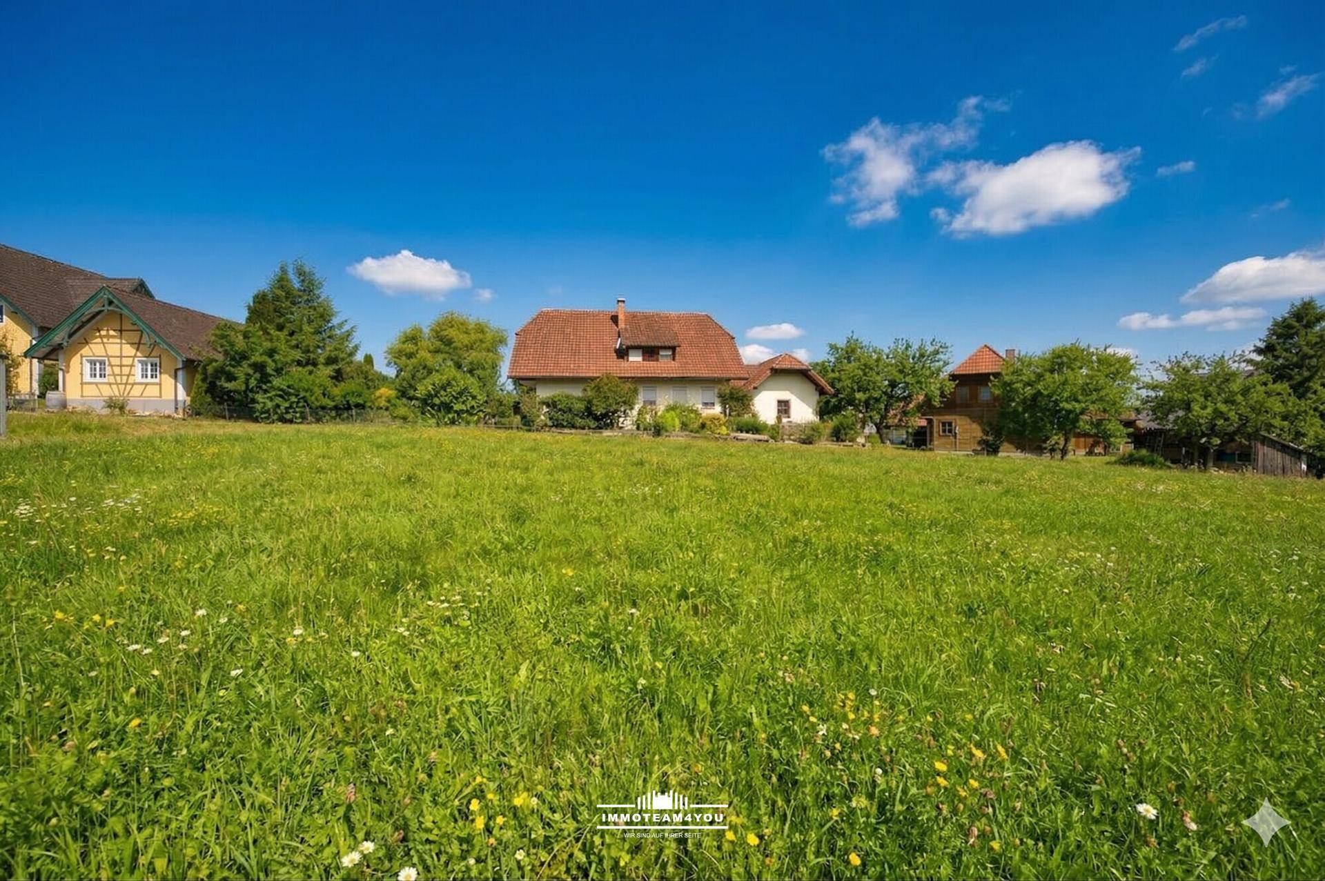 Idyllische Landschaft mit grünen Wiesen und traditionellen Häusern unter einem strahlend blauen Himmel.