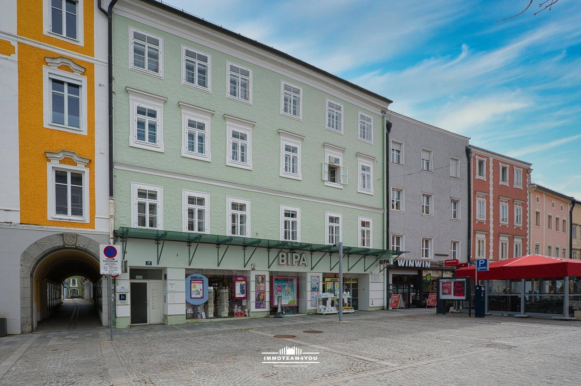 Historisches Gebäude mit Geschäften im Erdgeschoss und Wohnungen darüber, an einem belebten Stadtplatz gelegen.