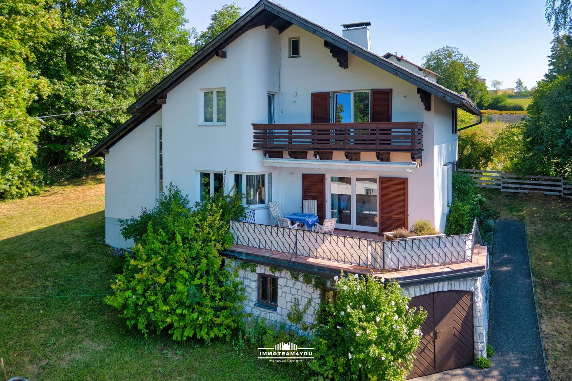 Vorderansicht des Hauses mit Balkonen, Garage und gepflegtem Vorgarten unter blauem Himmel.