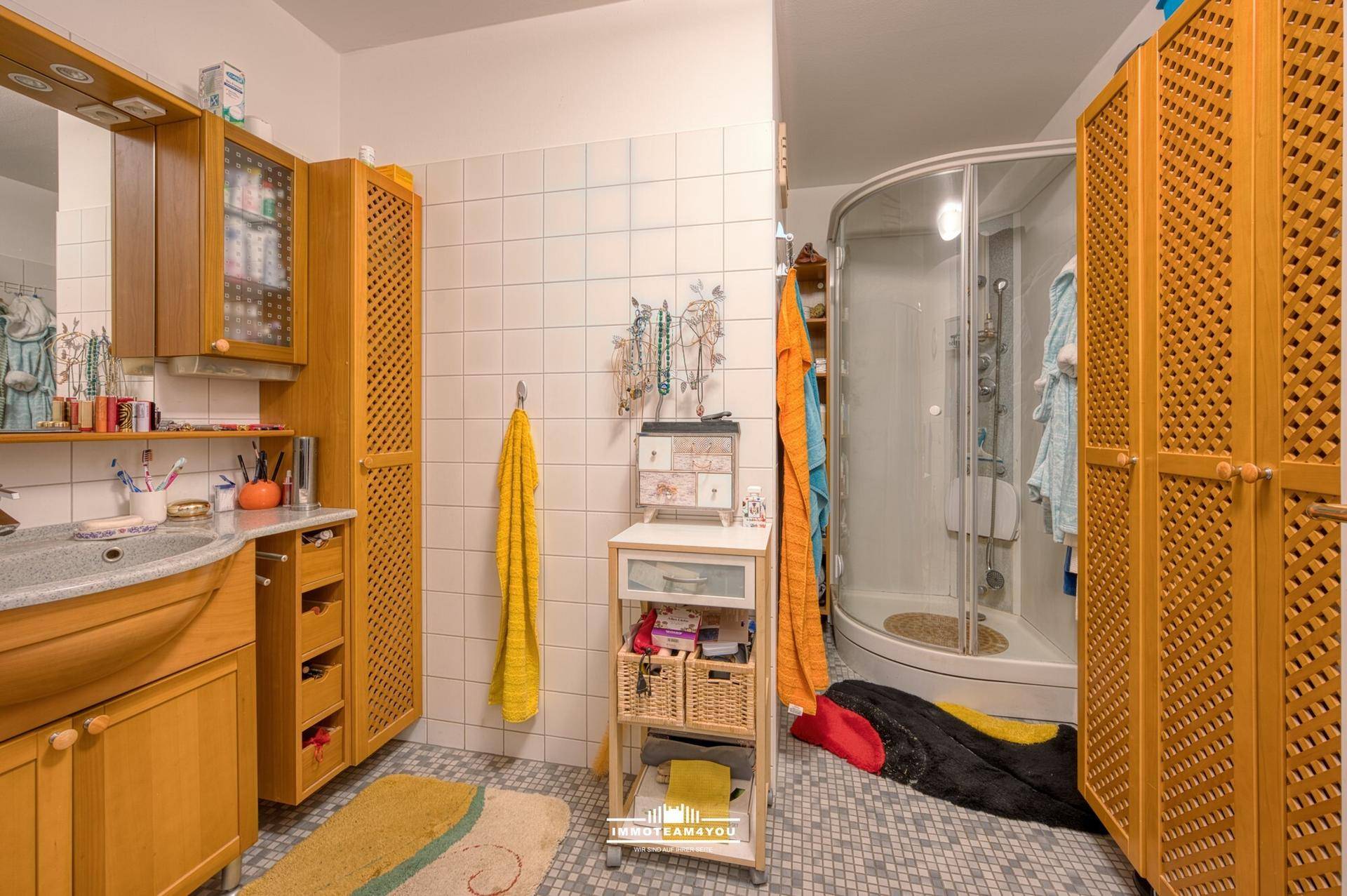 Badezimmer mit Duschkabine, Holzschränken und hellen Fliesen an den Wänden.