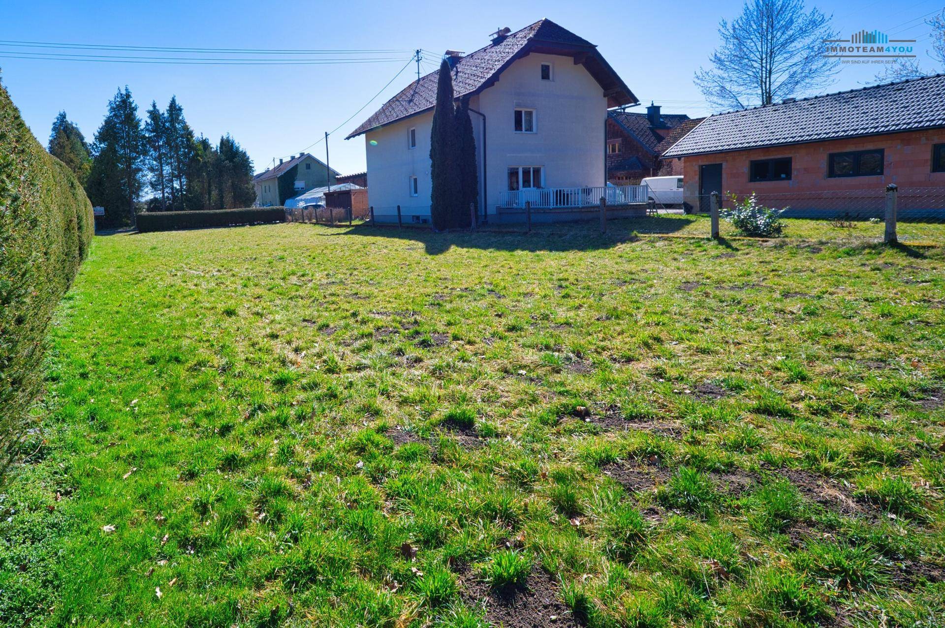 Weitläufige Rasenfläche mit einem Wohnhaus und einem Nebengebäude im Hintergrund an einem sonnigen Tag.