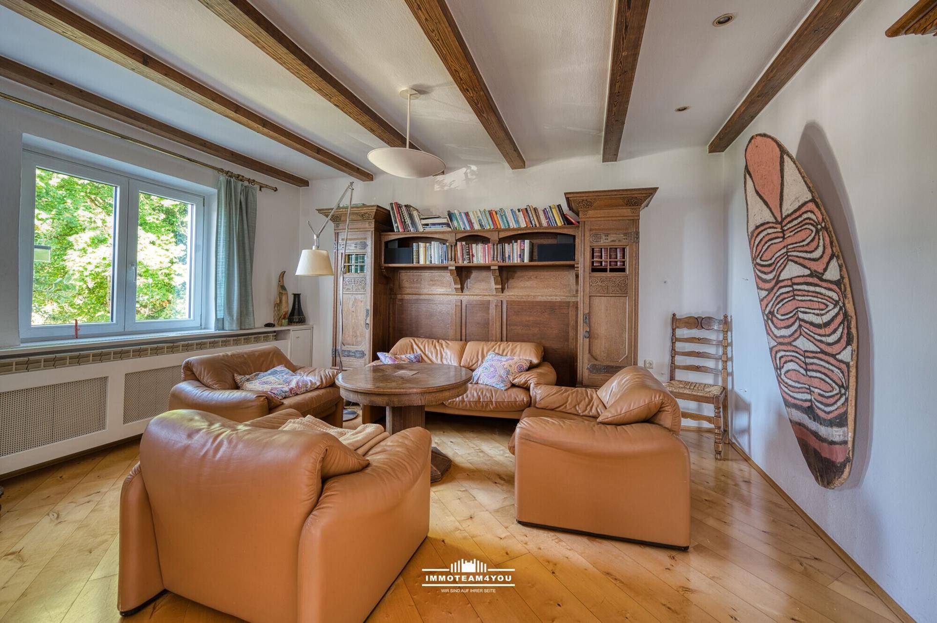 Geräumiges Wohnzimmer mit Ledersofas, Holzbalkendecke und großem Bücherregal.