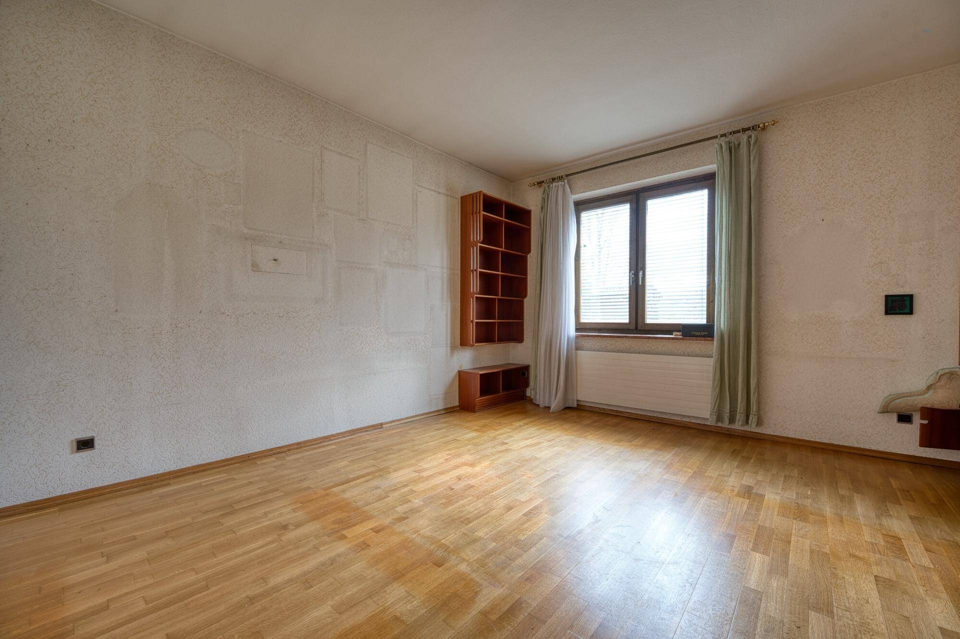 Geräumiges Schlafzimmer mit Holzboden, Fenster und einfacher Einrichtung, ideal für Gäste.