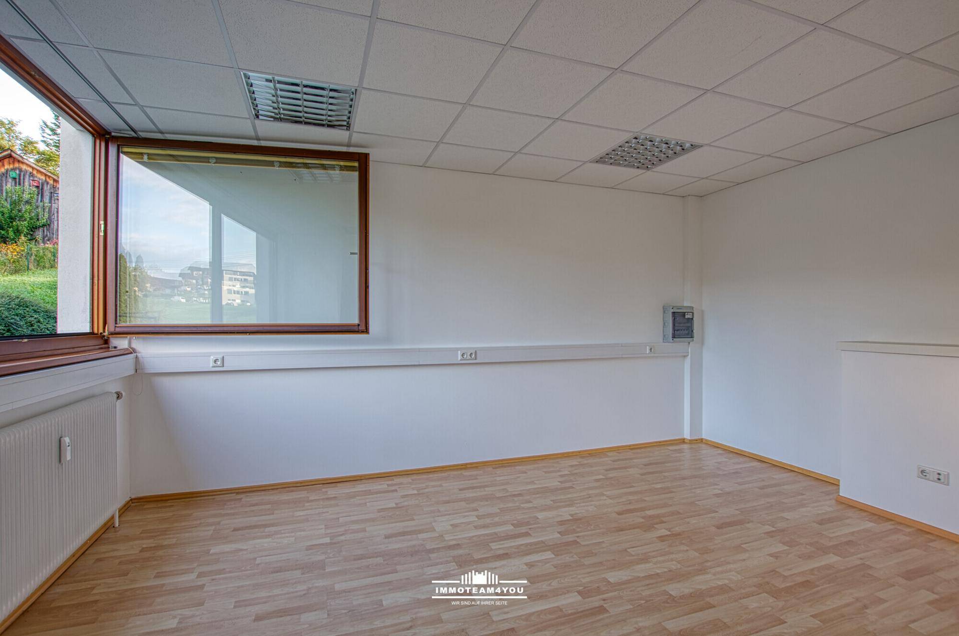 Heller Büroraum mit Laminatboden, großen Fenstern und einem weiten Blick auf die Umgebung.