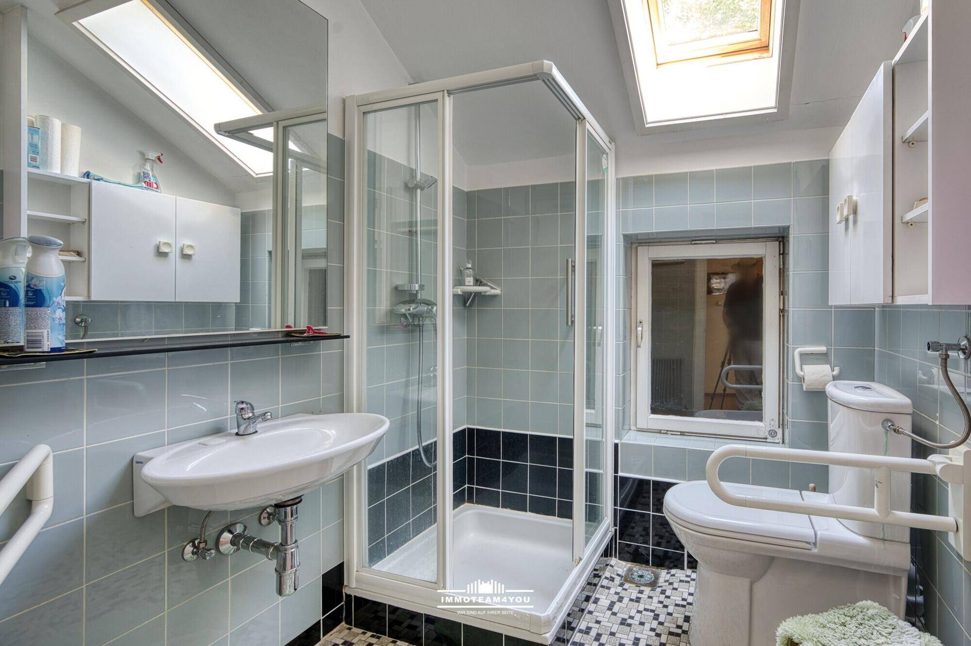 Helles Badezimmer mit Dusche, WC und Dachfenster, ausgestattet mit blauen Fliesen.