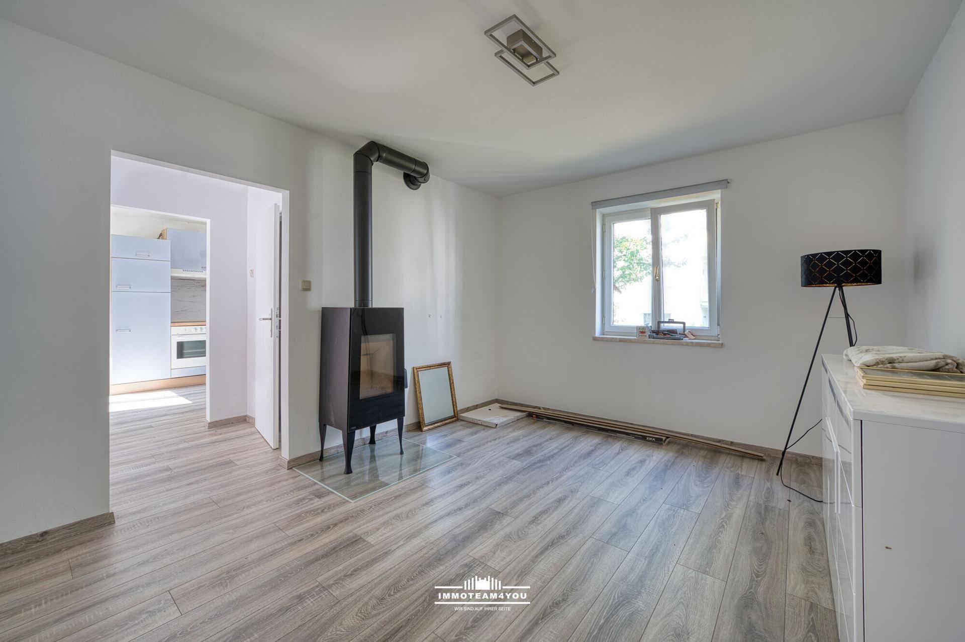 Leeres Wohnzimmer mit modernem Holzofen, Laminatboden und hellem Fenster.