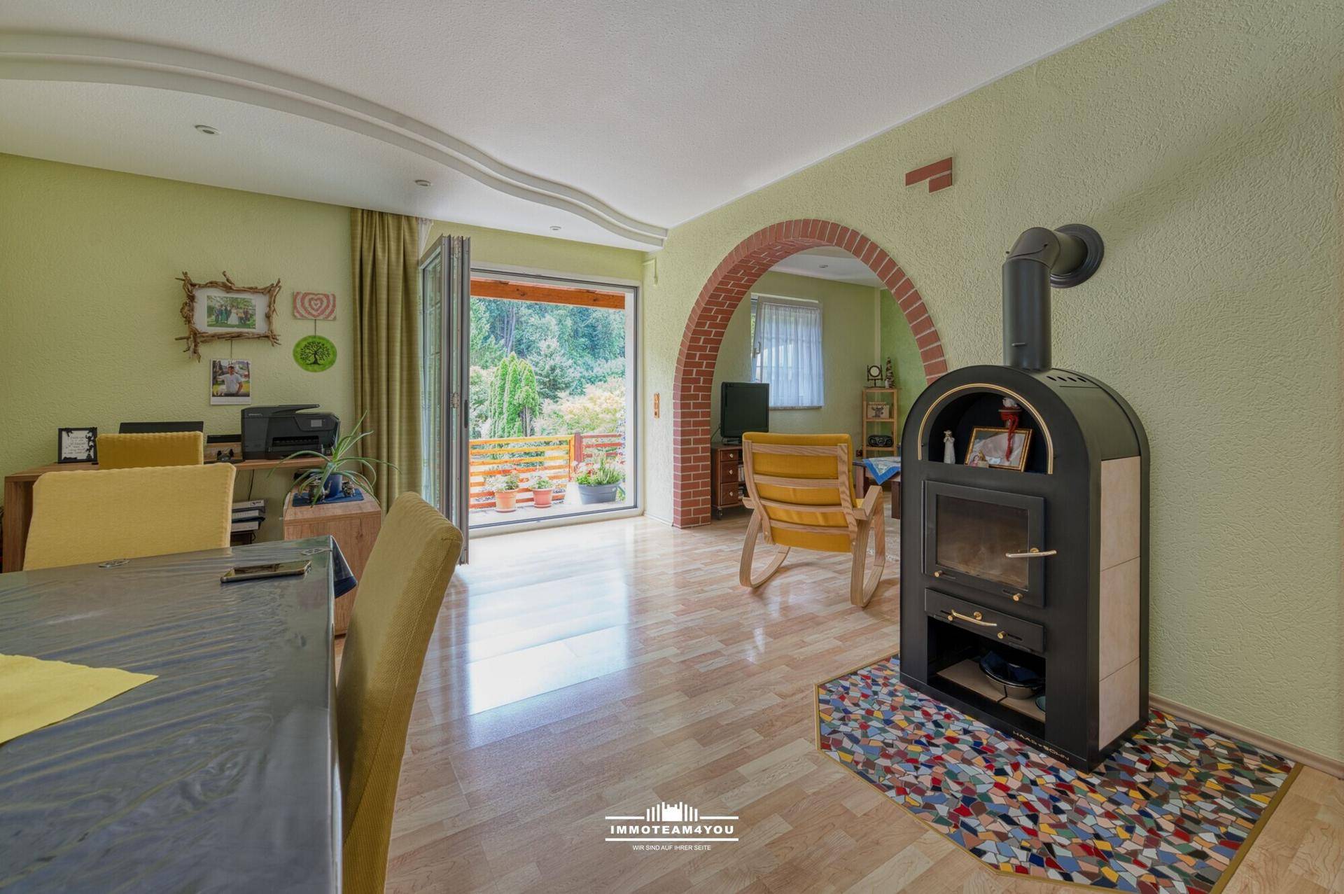 Heller Wohn- und Essbereich mit Holzboden, Kaminofen und Zugang zum Balkon.
