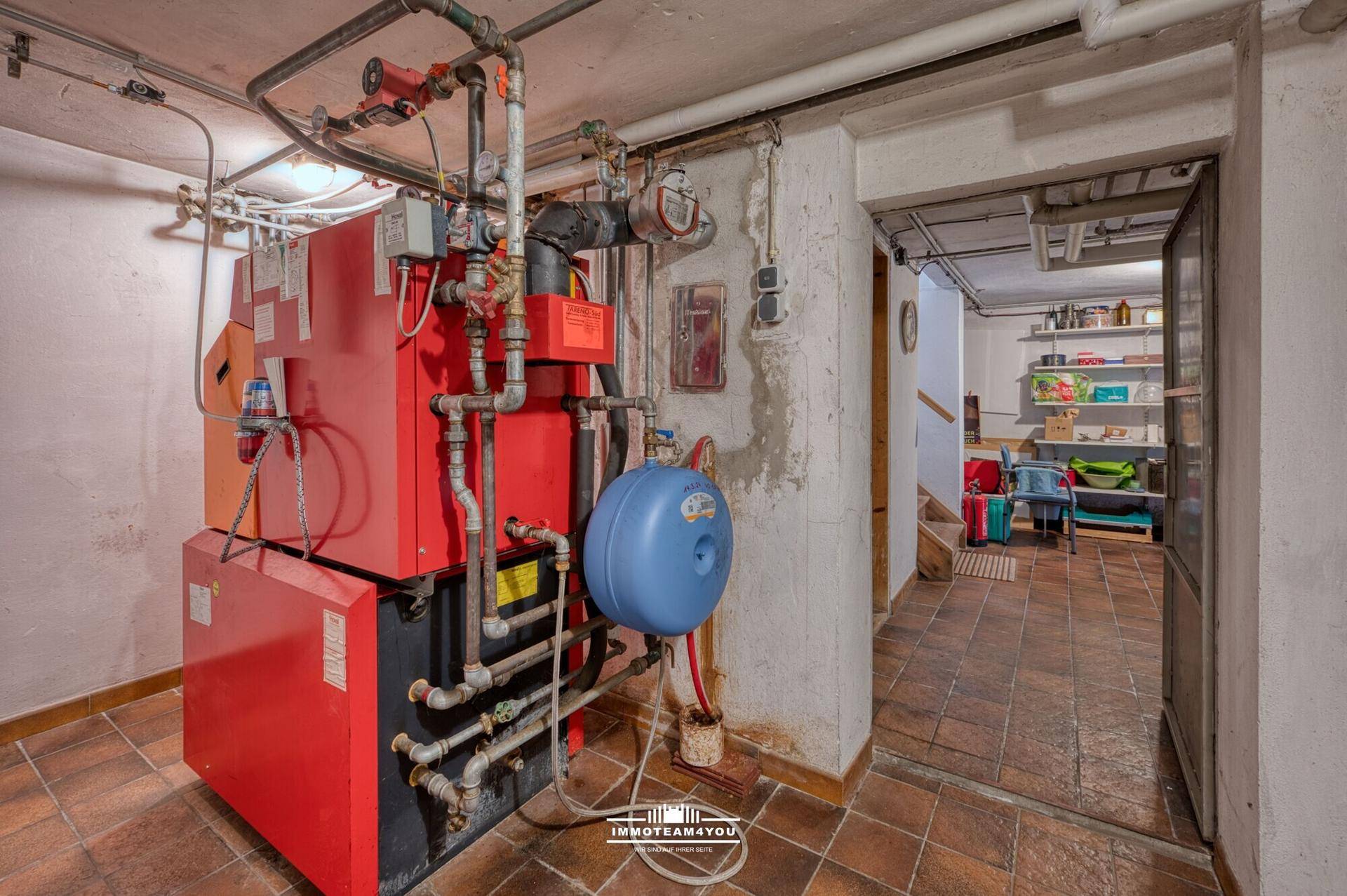 Heizungsraum im Keller mit großem Heizkessel und sichtbaren Rohrleitungen.