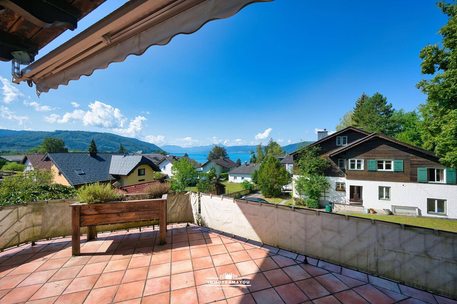 Geräumige Terrasse mit Terrakottafliesen, Holzpflanzkübel und weitem Blick auf den See.