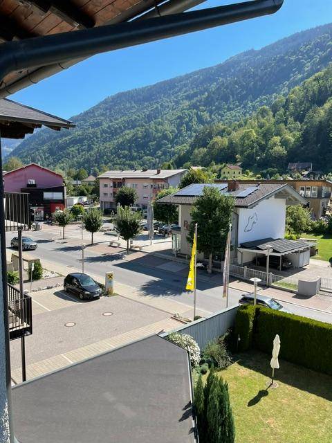 Weitblick über eine kleine Stadtstraße mit Gebäuden und grünen Bergen im Hintergrund.