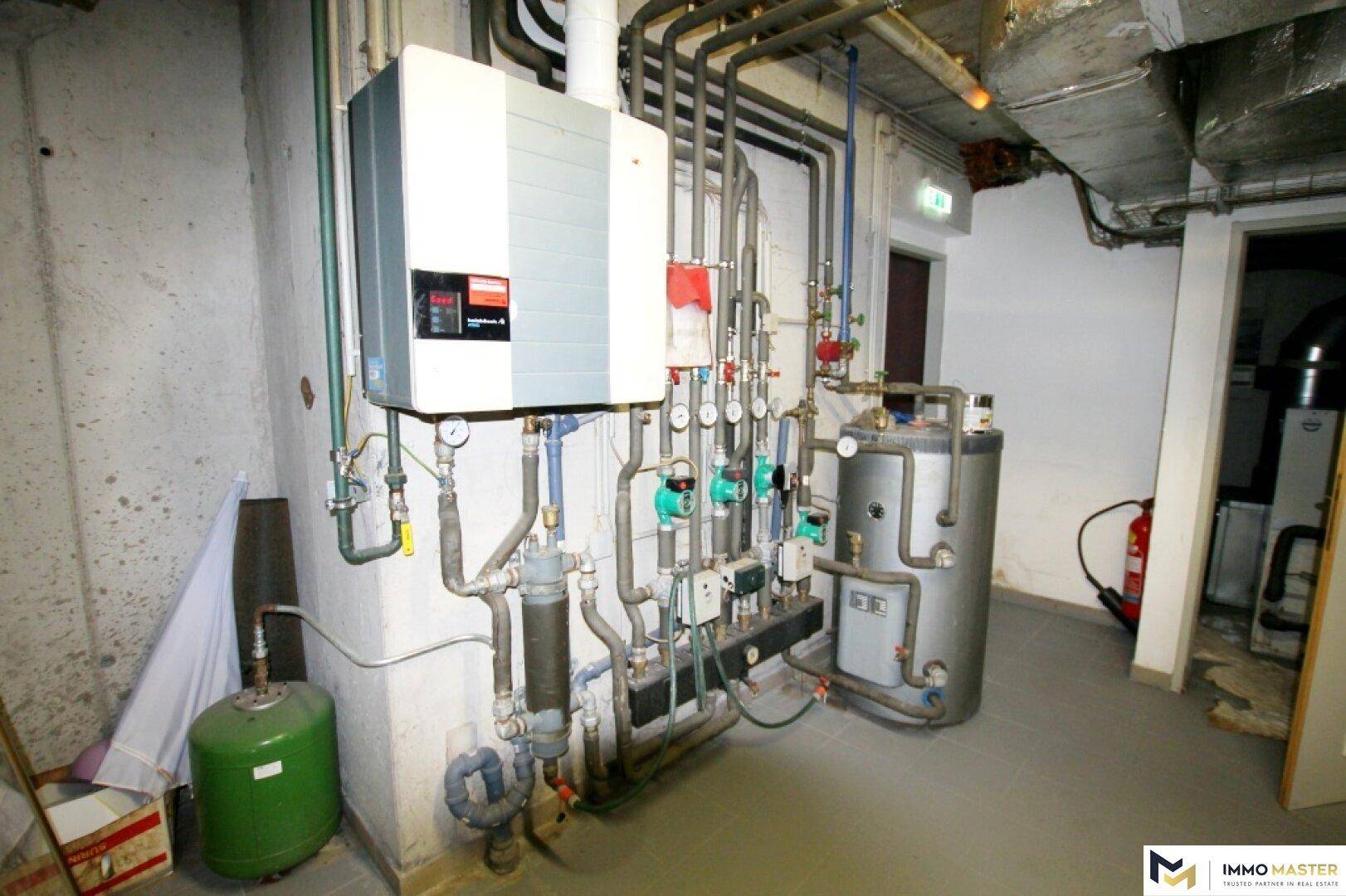 Heizungsraum mit mehreren Heizkesseln, Warmwasserspeicher und komplexen Rohrleitungen.