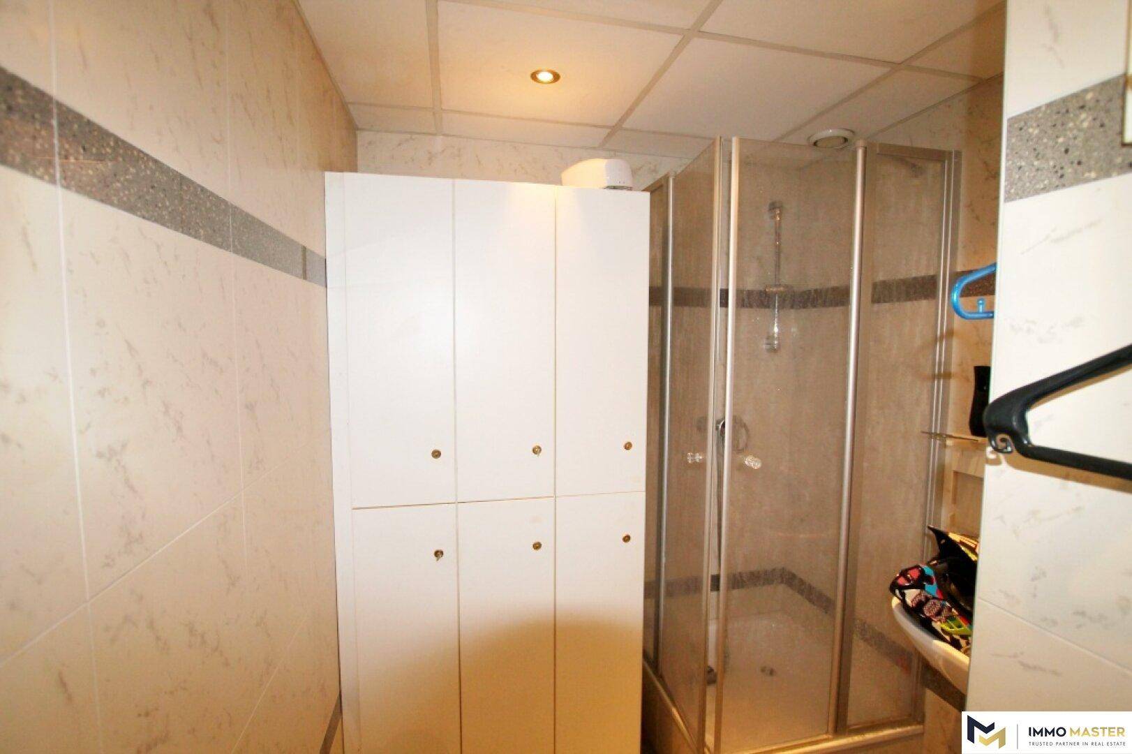 Badezimmer mit Duschkabine, weißen Schränken und hellen Fliesen an den Wänden.