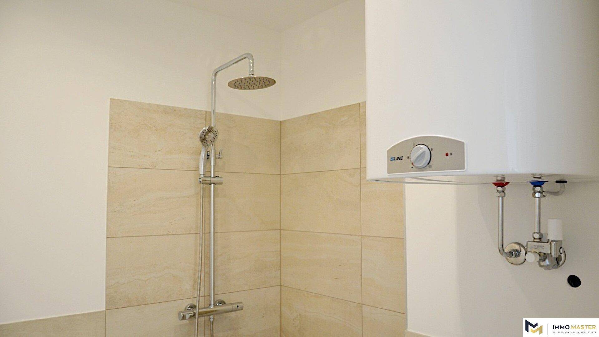 Modern geflieste Dusche mit Regenduschkopf und einem Warmwasserboiler an der Wand.