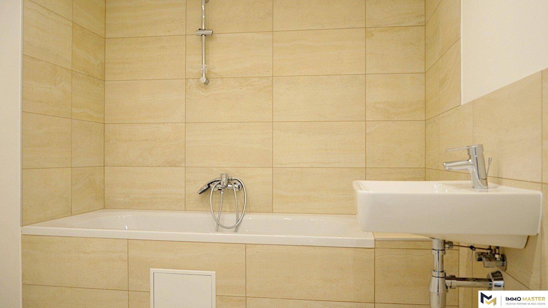 Helles Badezimmer mit Badewanne, modernem Waschbecken und beigefarbenen Fliesen.