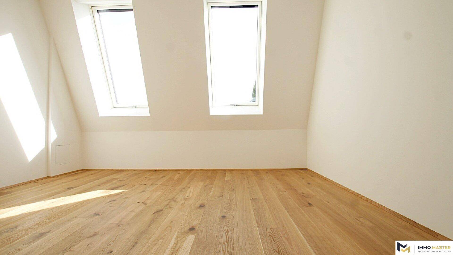 Geräumiges Dachzimmer mit Holzboden und zwei hellen Dachfenstern, ideal für ein Schlafzimmer.