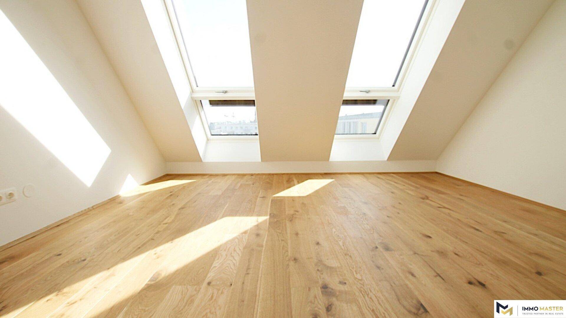 Heller Dachgeschossraum mit Holzboden und zwei großen Dachfenstern, die viel Licht spenden.
