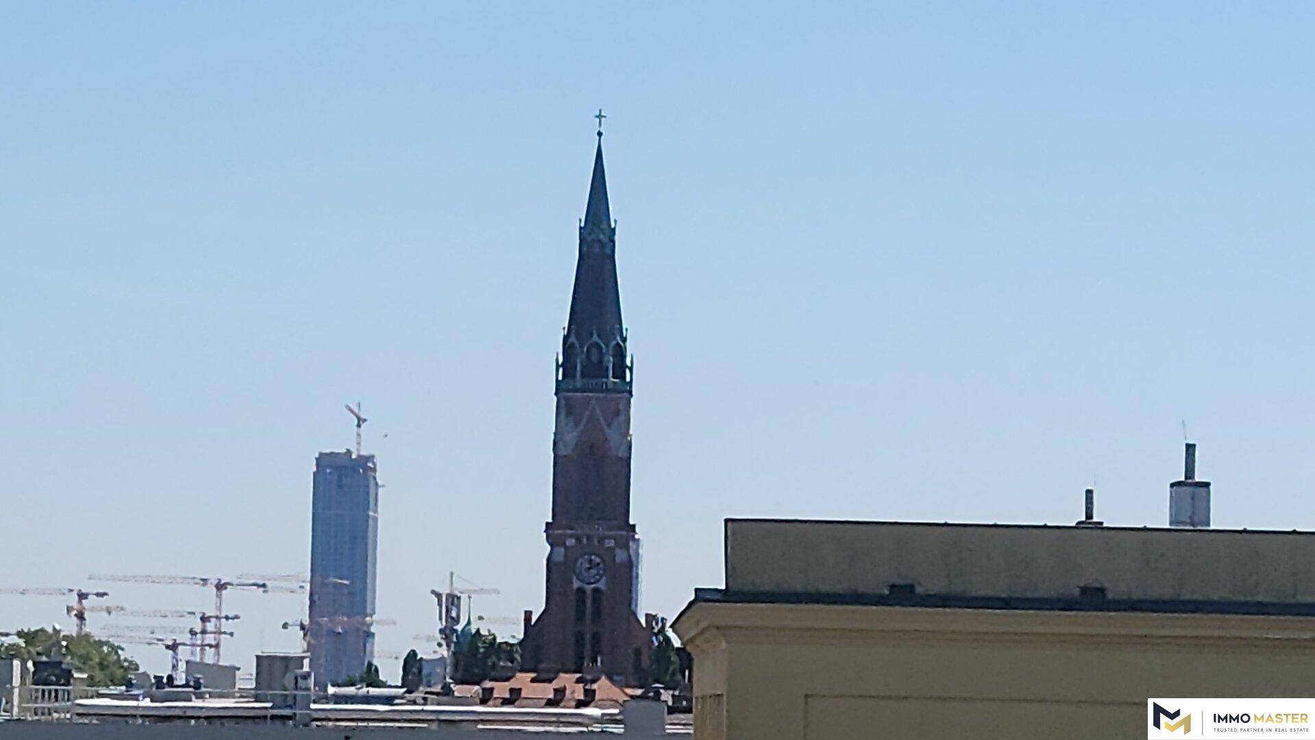 Stadtansicht mit einer historischen Kirchturmspitze und modernen Gebäuden im Hintergrund.