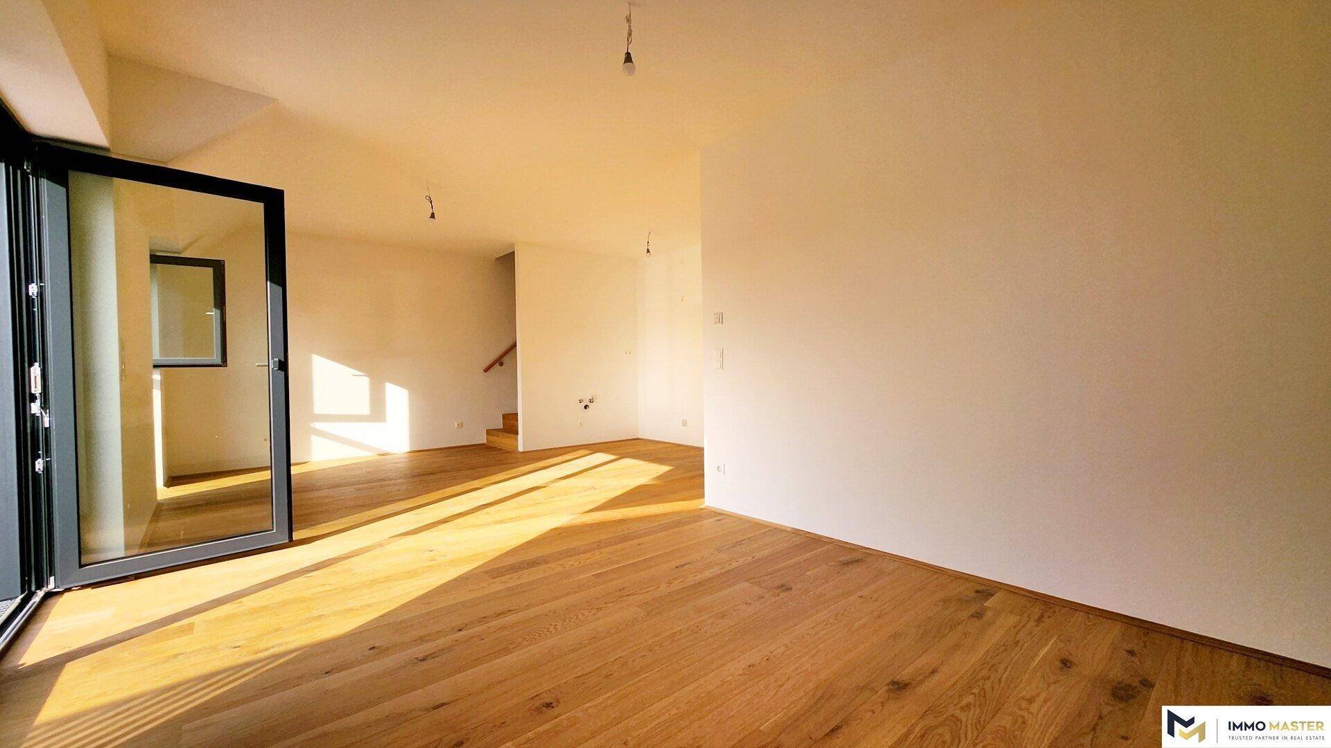 Geräumiger Wohnbereich mit Holzboden, viel Tageslicht und Blick auf die Innentreppe.