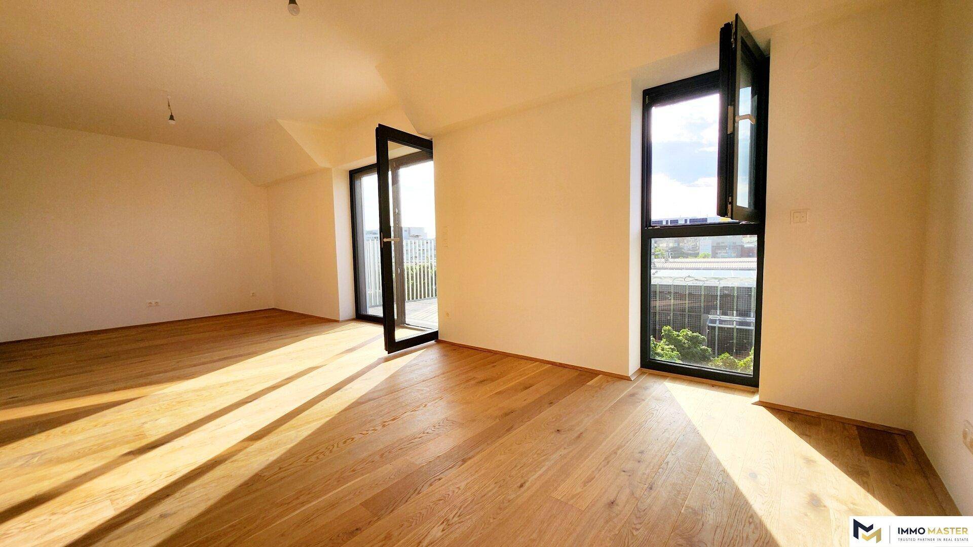 Geräumiger, heller Raum mit Holzboden und mehreren Fenstern, die viel Tageslicht hereinlassen.