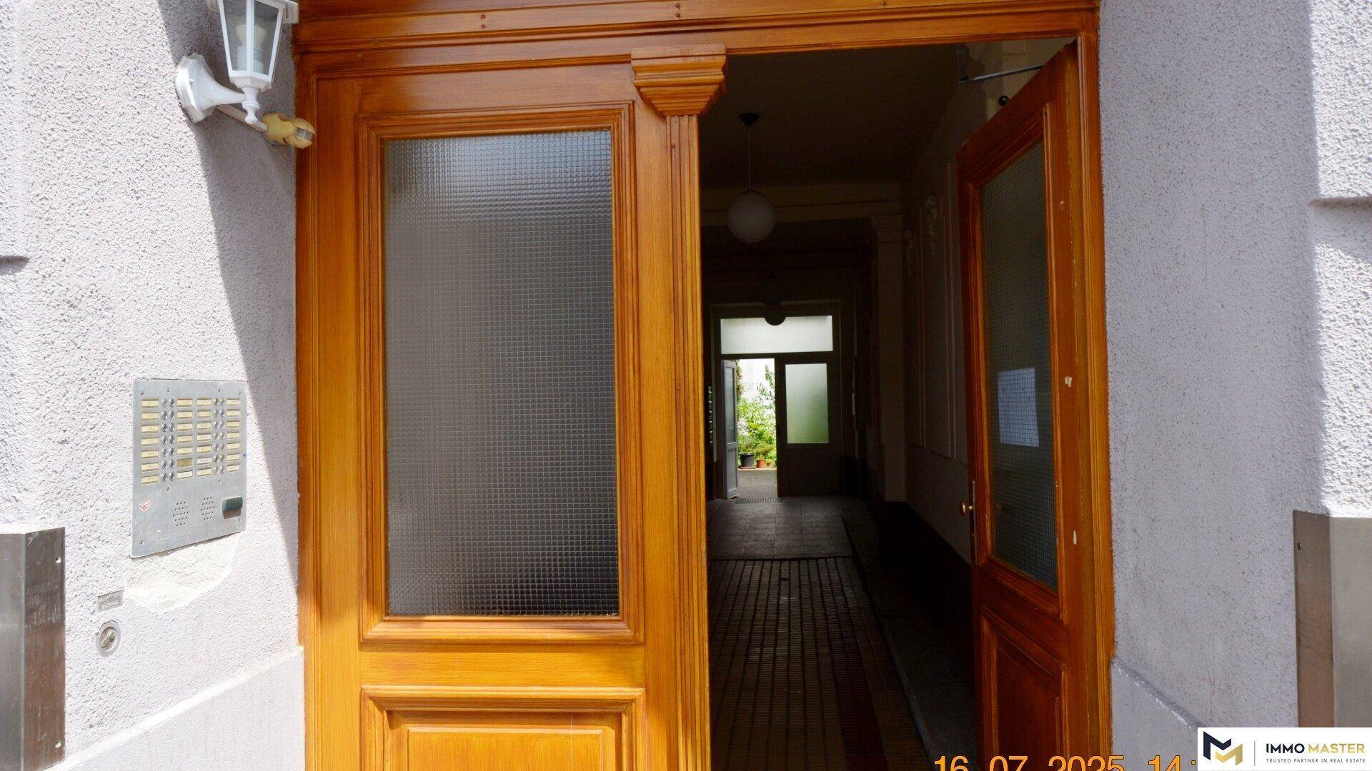 Eingangstür aus Holz mit Glasausschnitt und Klingelanlage, die zum Gebäude führt.