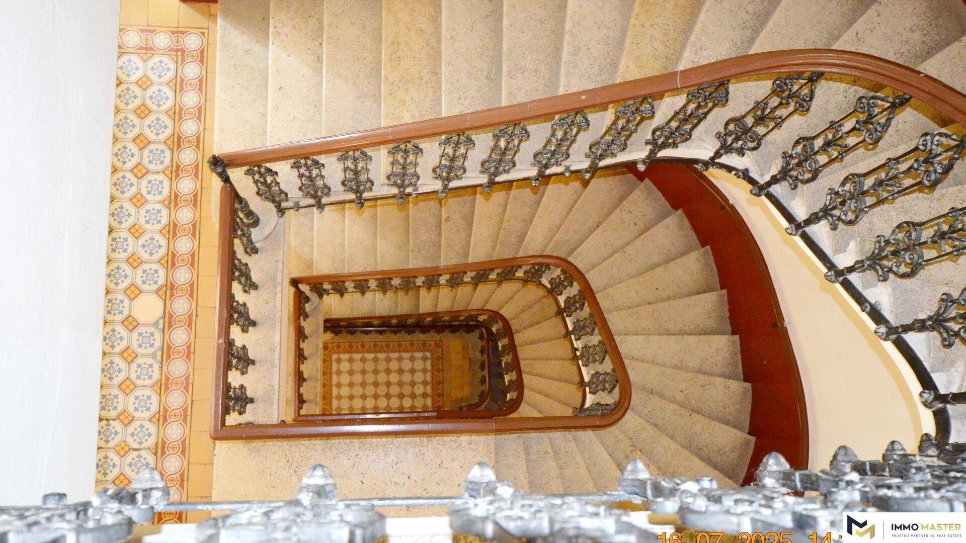 Historisches Treppenhaus mit kunstvollem Geländer und gemusterten Fliesen, von oben gesehen.