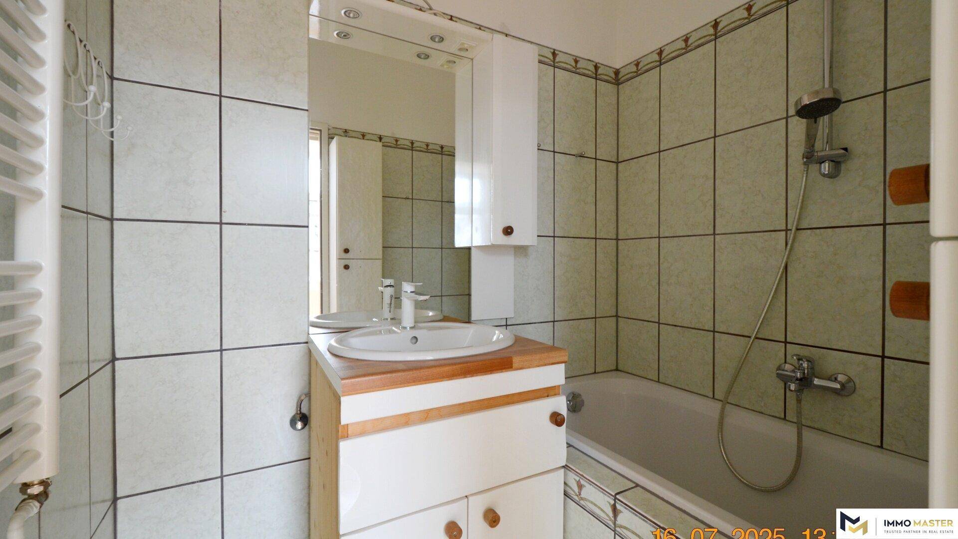 Badezimmer mit Waschbecken, Spiegel und Badewanne, ausgestattet mit hellen Fliesen.