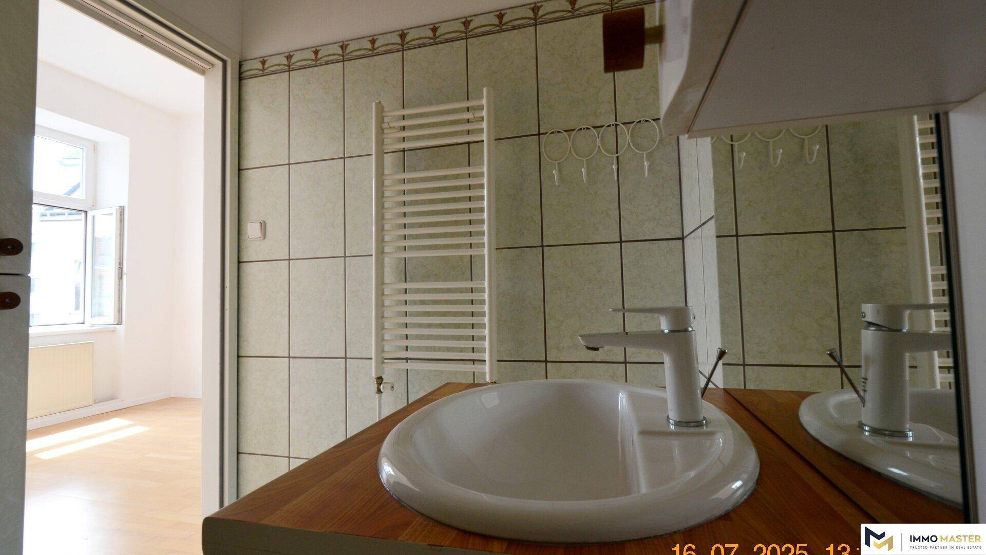 Waschbecken mit Spiegel und beheiztem Handtuchhalter in einem hell gefliesten Badezimmer.