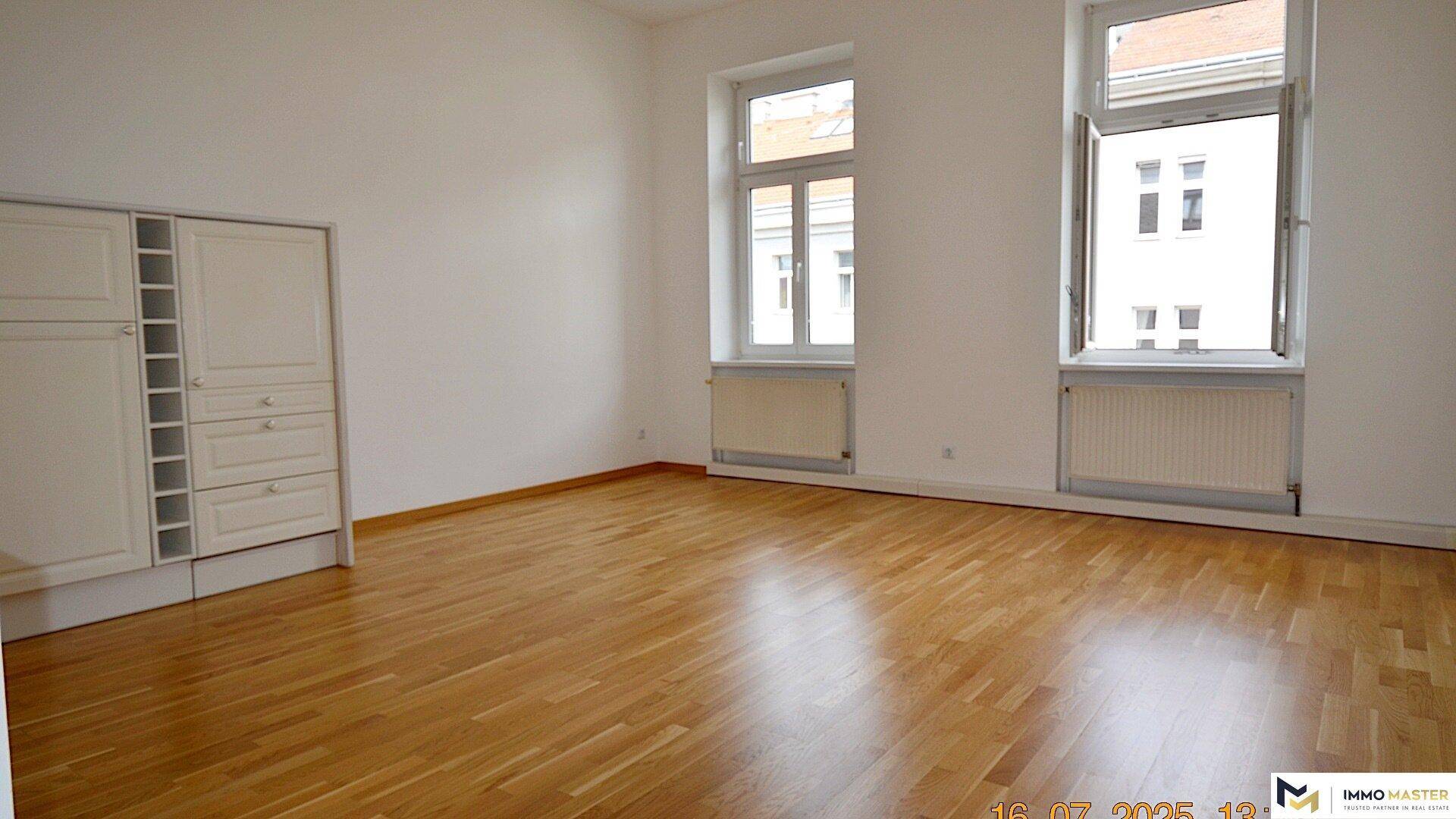 Wohnzimmer mit Holzboden und zwei Fenstern, die den Raum hell und freundlich wirken lassen.