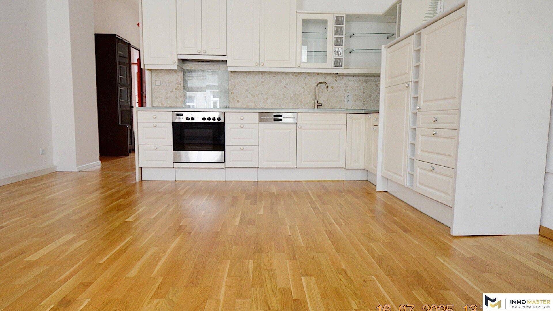 Helle Einbauküche mit weißen Schränken, Backofen und Holzboden in offenem Wohnbereich.