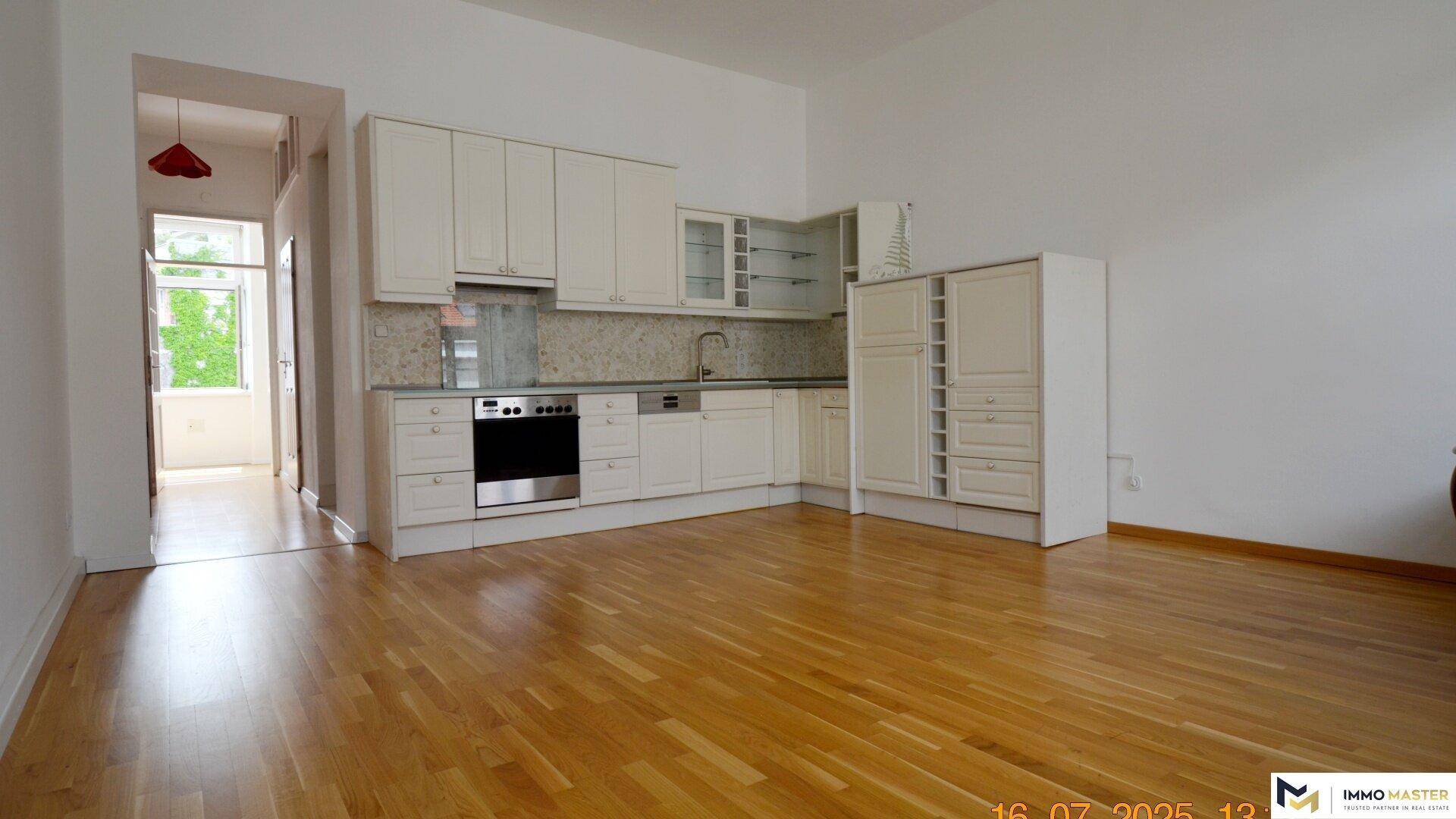 Offene Küche mit Holzboden und weißer Einbauküche, angrenzend an einen Wohnbereich.